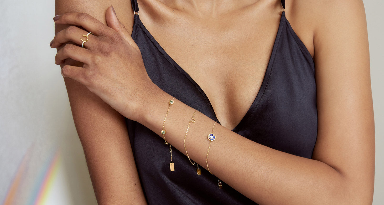 A model wears a stack of Canadian-made 18K yellow gold bracelets with emeralds, sapphires, and diamonds, and a diamond ring.