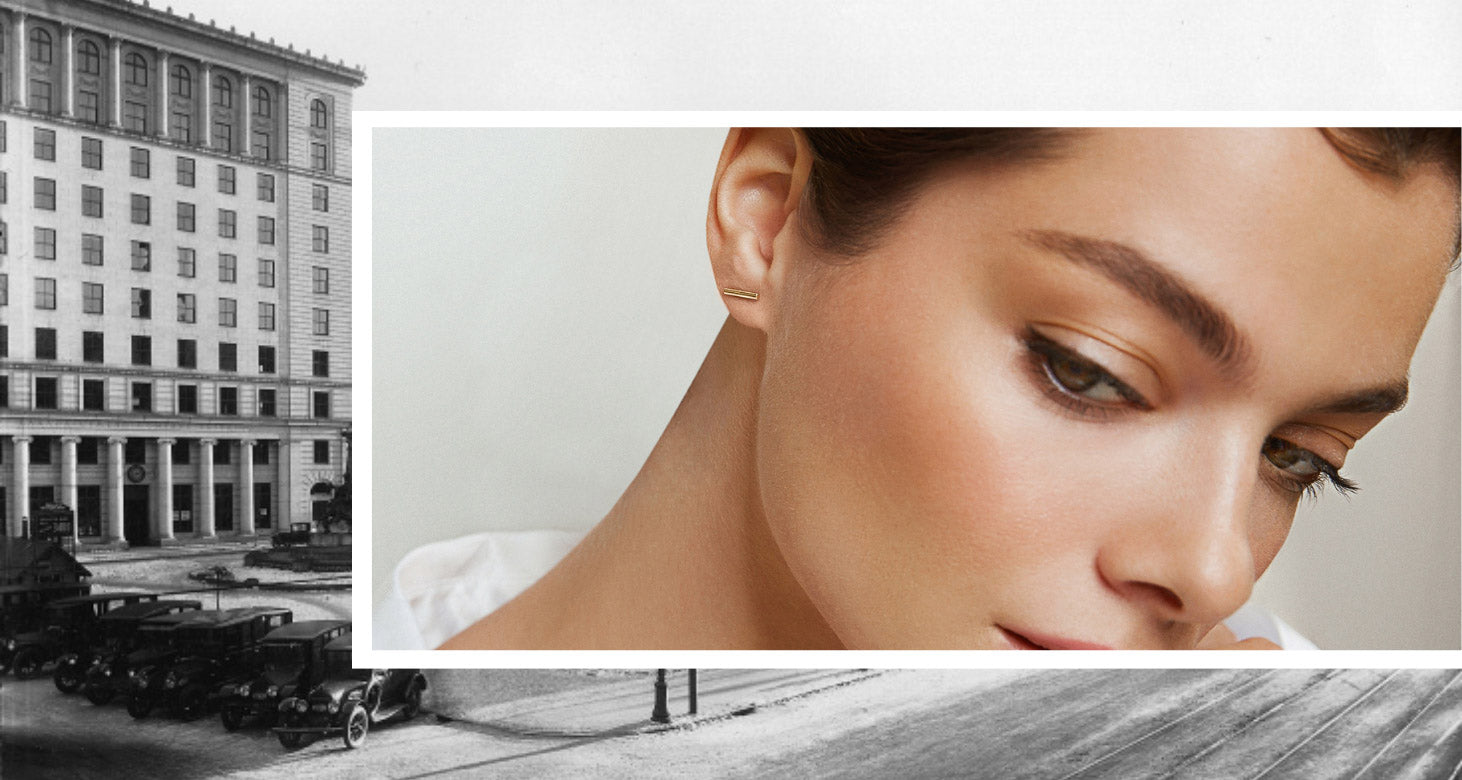 Modern 18K yellow gold bar stud earring on a model, with a backdrop of historic Montreal. Canadian-made by Jewellers District.