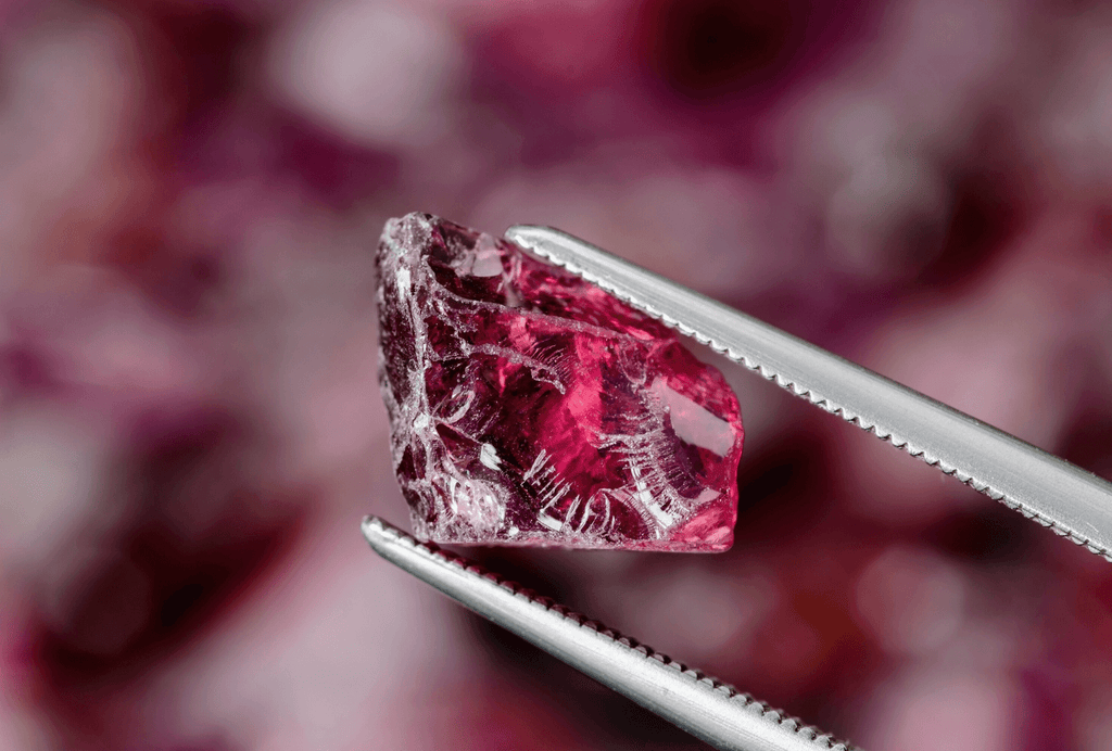 A raw ruby gemstone held in tweezers, ready to be set in a custom Canadian-made engagement ring.