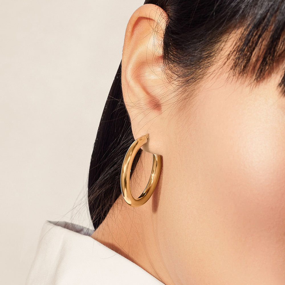 Model wearing Jewellers District's Thick Gold Hoop Earrings in 10k Yellow Gold